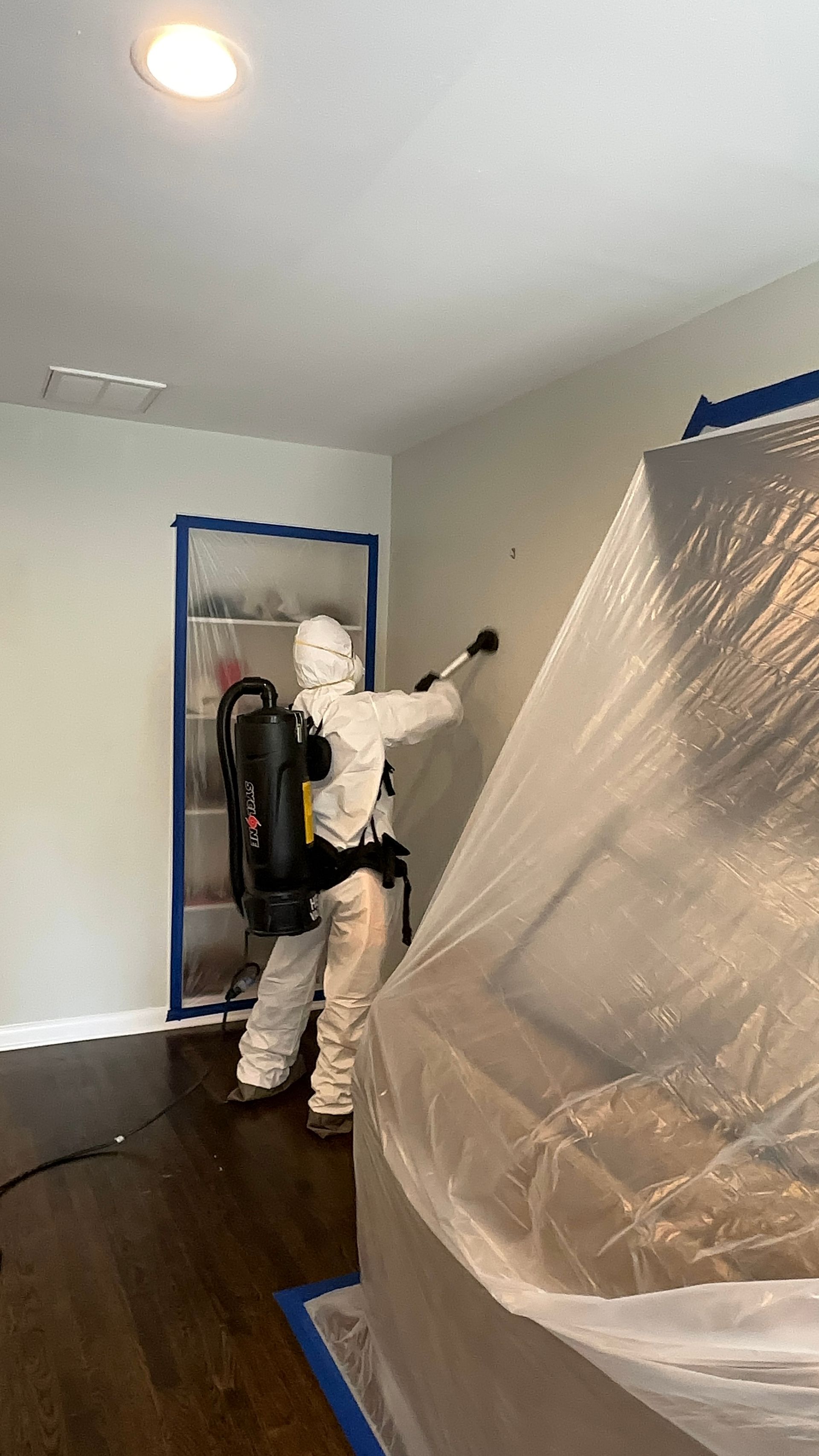A restoration technician in full protective clothing cleans an interior wall using specialized equip 