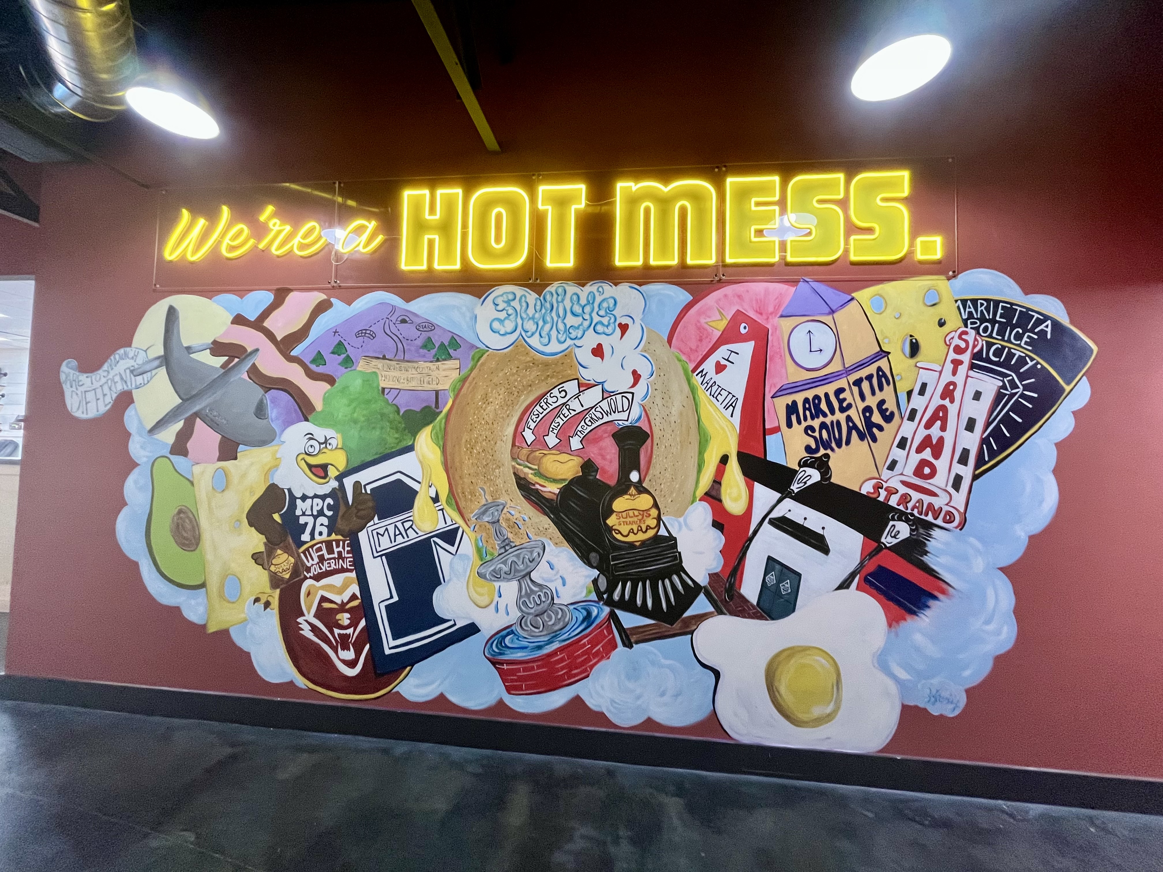 Our &ldquo;Hot Mess&rdquo; mural, created by local artist, Jill Hooley, celebrates the spirit of Marietta with nods to hometown landmarks and Sully&rsquo;s signature sandwiches.