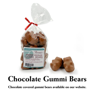 This photograph showcases a bag of Florence's Exquisite Chocolates' "Premium Chocolate Gummi Bears," likely from their Rexburg, Idaho location. The clear bag allows the chocolate-covered gummi bears to be clearly seen, tied with a festive red ribbon. The product label identifies them as "Premium Chocolate Gummi Bears" and includes a barcode. Several loose chocolate-covered gummi bears are scattered beside the bag, revealing their detailed bear shape and milk chocolate coating. Below the image, text clarifies that these "Chocolate covered gummi bears"