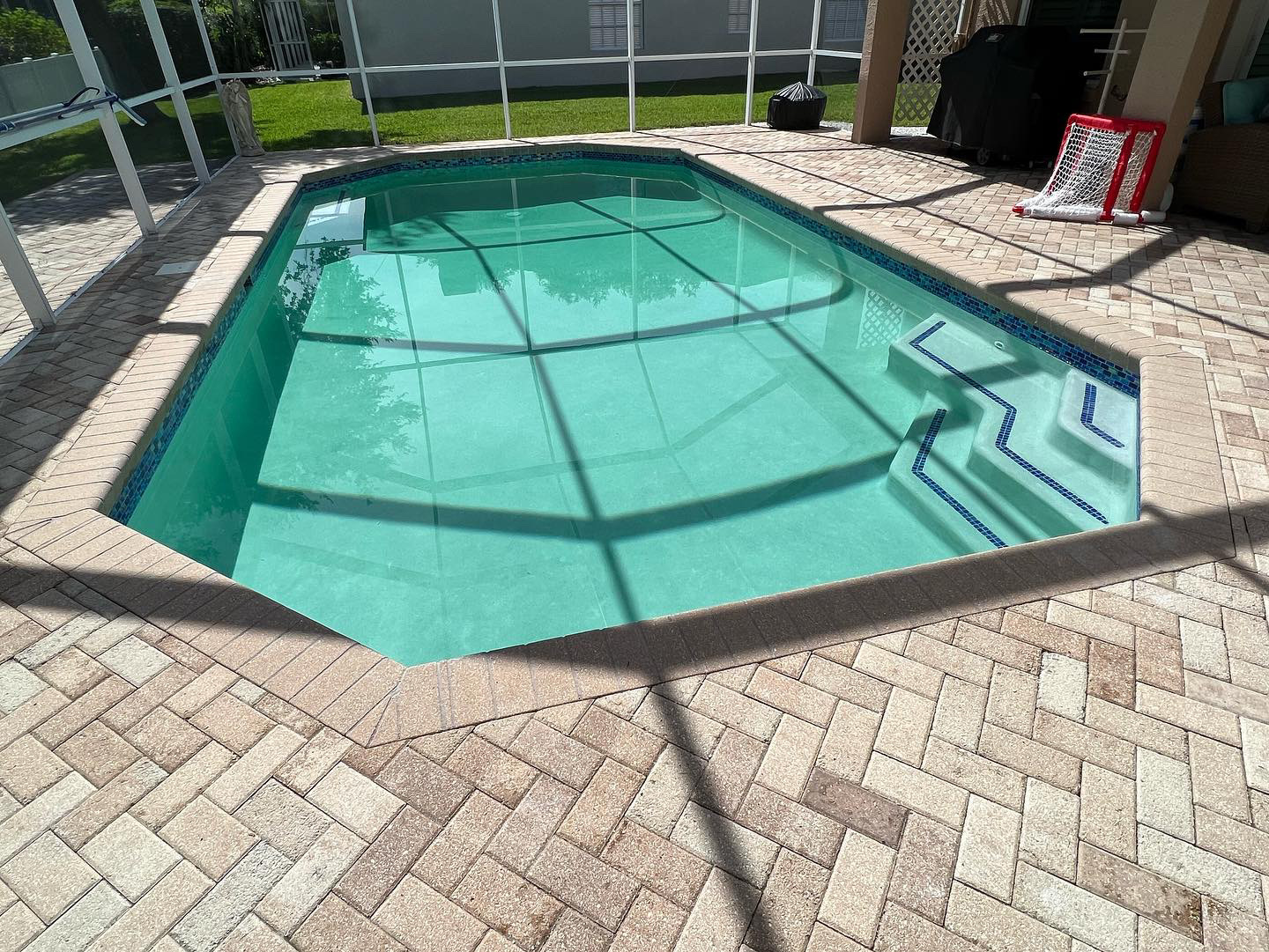 Screen-enclosed residential swimming pool with turquoise water, built-in entry steps, and brick paver decking.