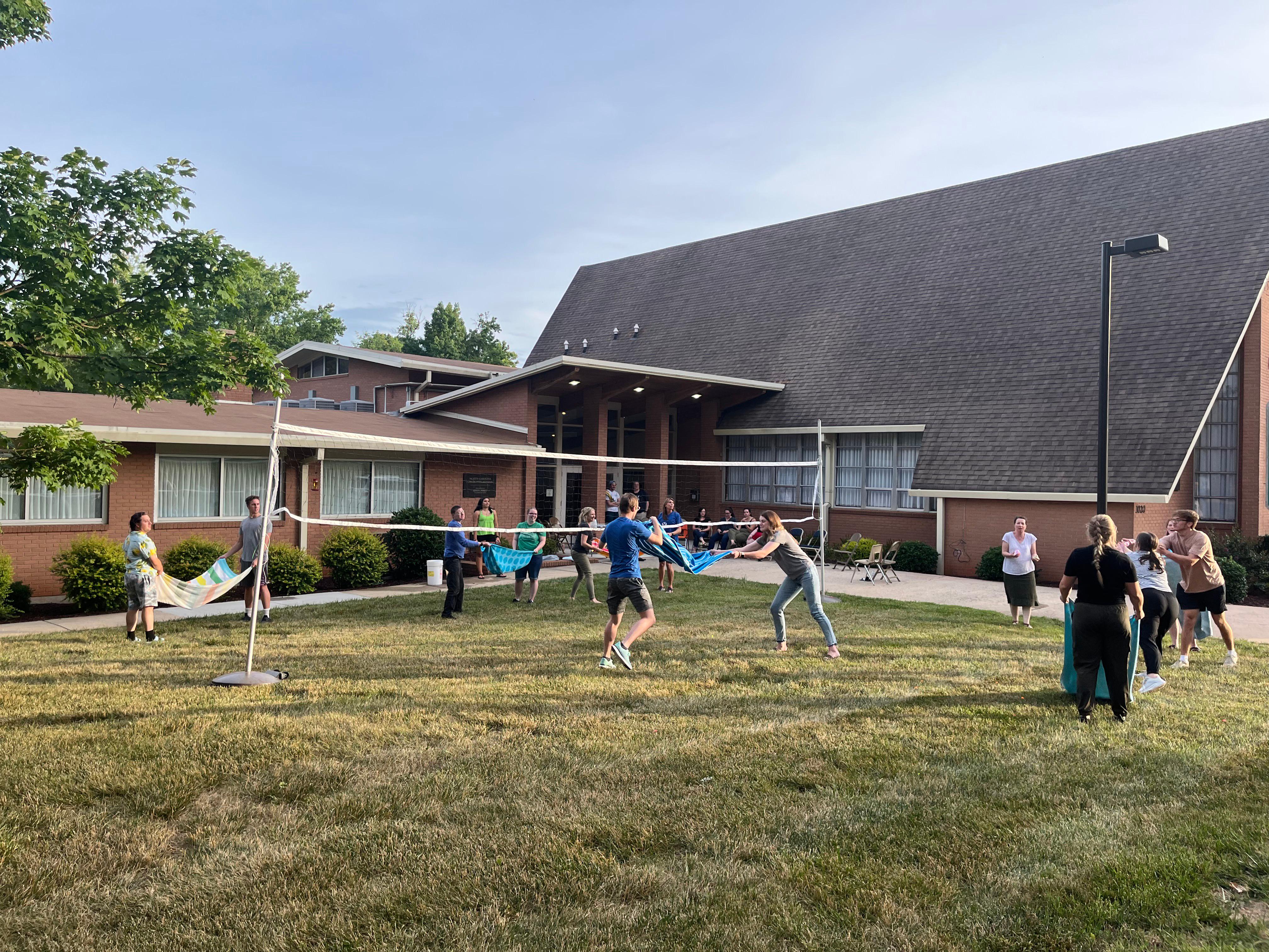 Young single adults play volleyball outside of the church building.