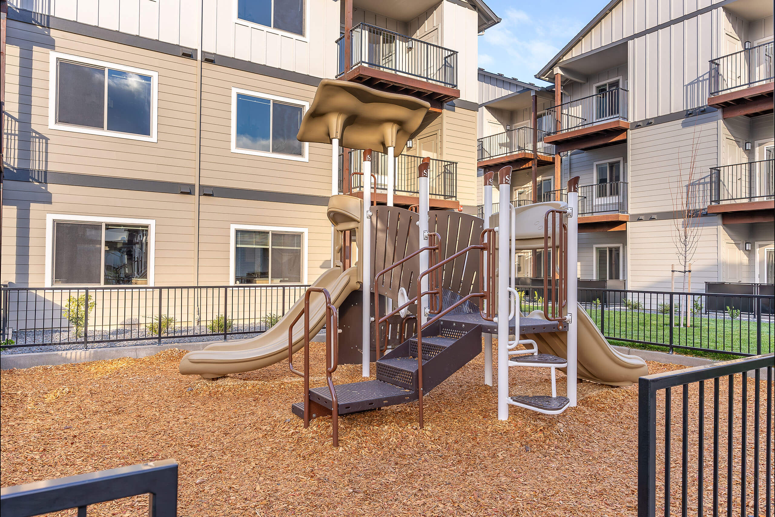 A playground with a slide and a climbing frame in front of apartment buildings.