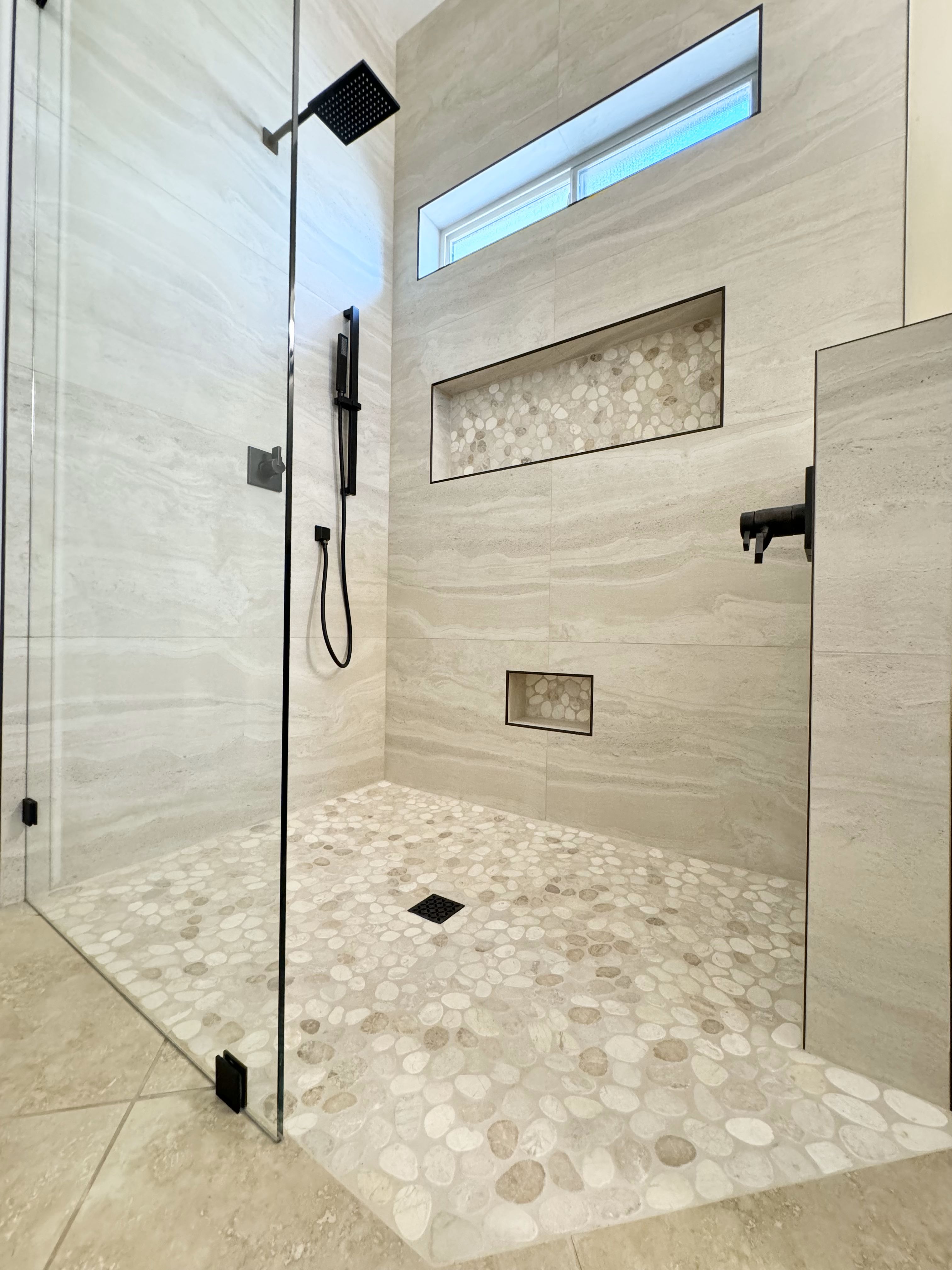 This stunning design features a spacious walk-in shower with sleek glass doors, natural pebble flooring, and stylish built-in niches for functionality and style. Whether you're looking for a complete bathroom remodeling project or a luxurious shower upgrade, Ledezma Remodeling delivers top-tier craftsmanship for your home renovation needs.