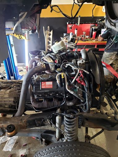 Vehicle chassis with exposed engine and suspension components in workshop. Mechanic tools and parts are visible around, indicating ongoing repair or assembly process, showcasing detailed mechanical work required for vehicle restoration and performance optimization.
