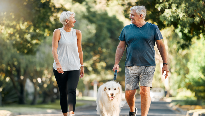 An older couple with a dog walking outside.