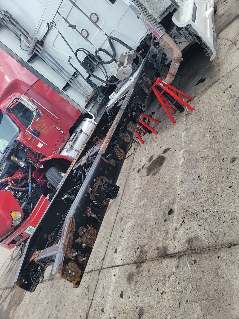 This high-angle shot shows a long, black semi-truck chassis frame supported by red jack stands on a  