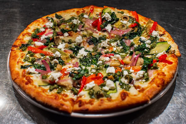 Veggie pizza with a hand-tossed crust with basil pesto and garlic, topped with roasted red peppers, red onion, artichoke hearts, mushrooms, Spanish green olives, zucchini, sautéed spinach, and goat cheese..