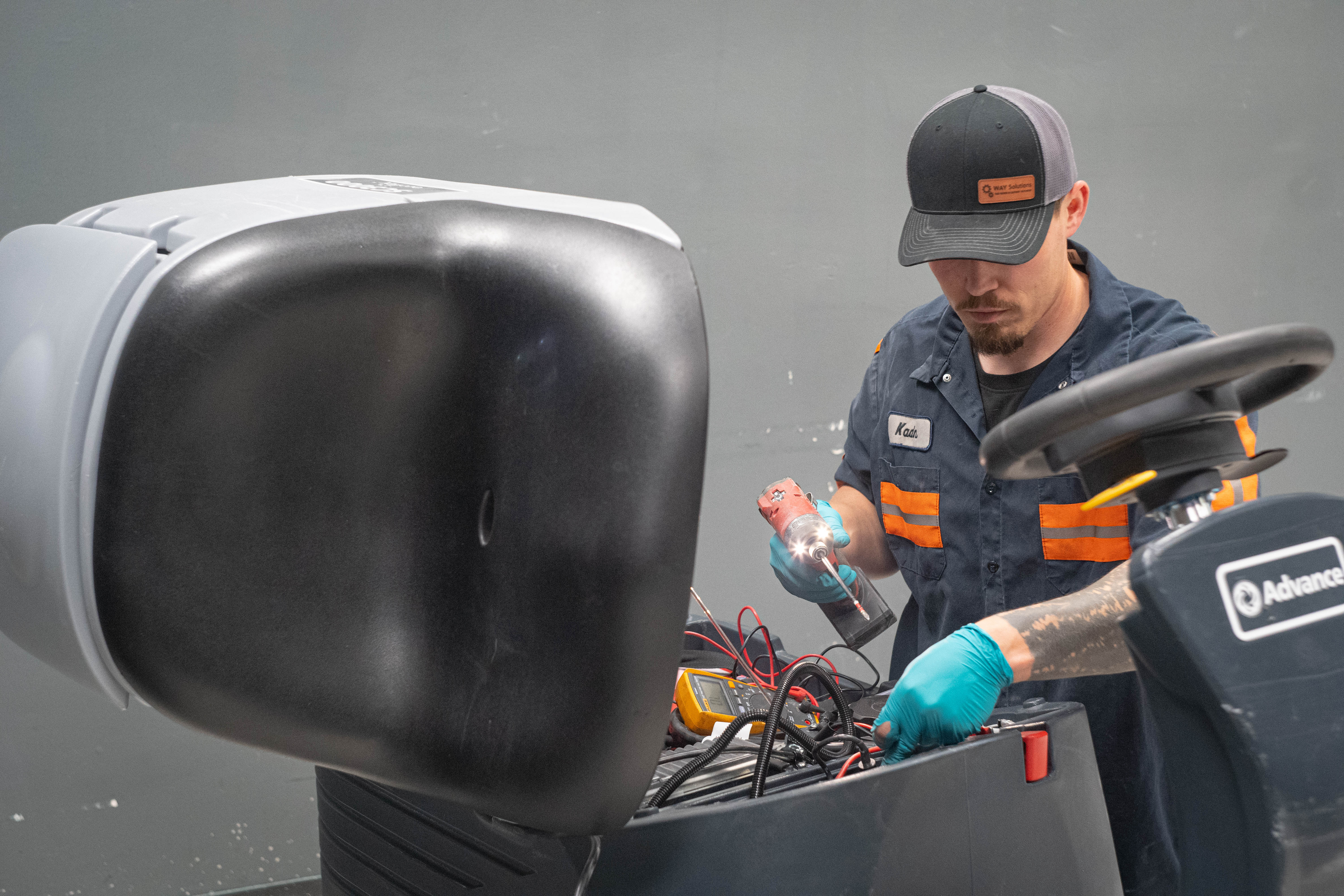 An expert WaySolutions technician utilizes a digital multimeter to trace and diagnose complex electrical wiring faults on a commercial floor scrubber's main control board. Our Layton, Utah team specializes in advanced electrical repairs to resolve error codes and restore full functionality to industrial cleaning fleets.