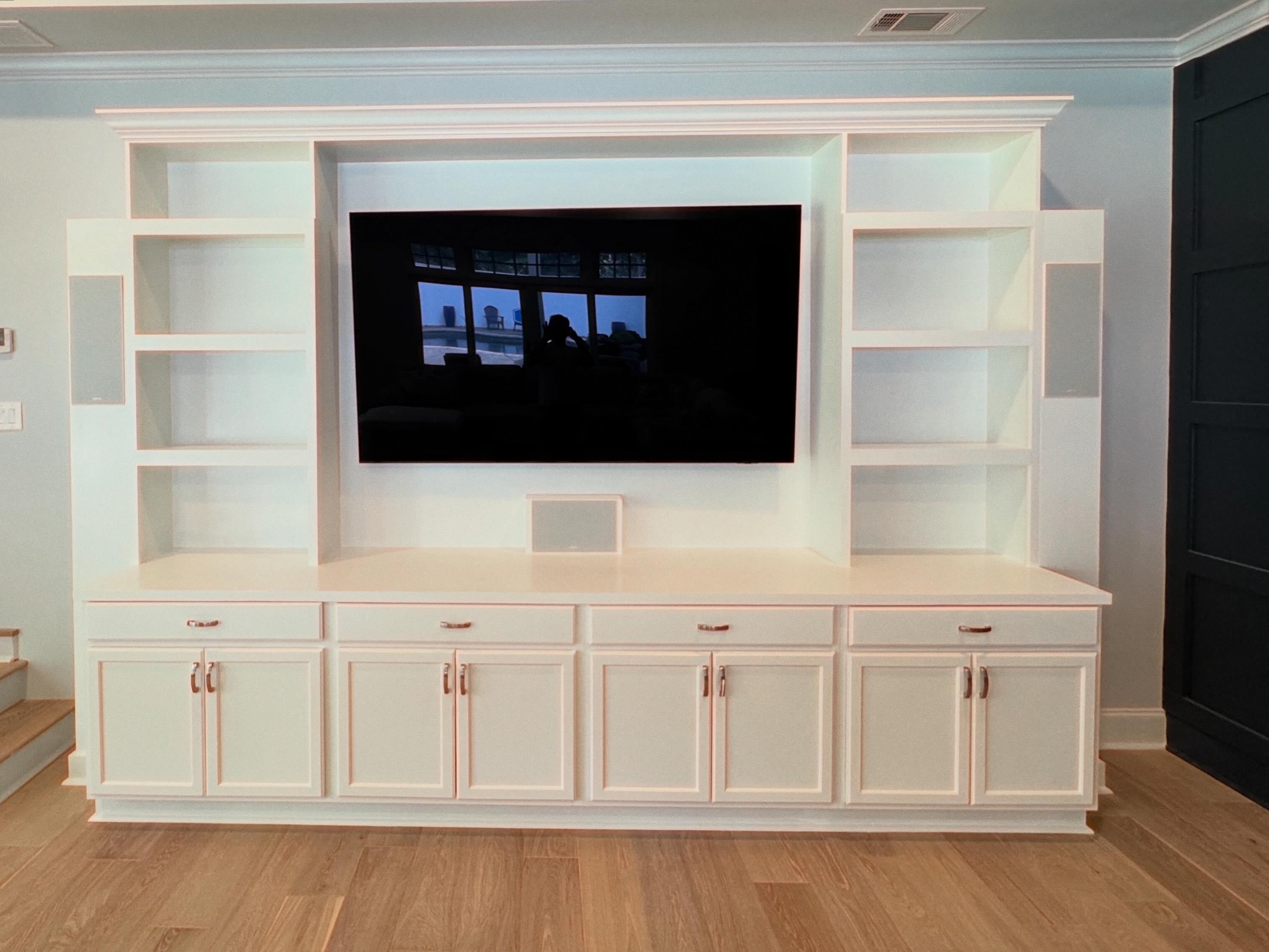 White custom built-in entertainment center with cabinets, open shelves, trim molding, and mounted TV space in a finished living room.
