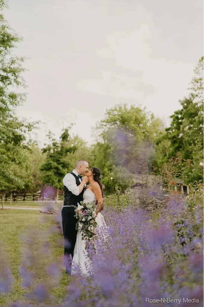 wedding photo of bride and groom kissing in a field with what looks like lavender out of focus adding depth to the shot.