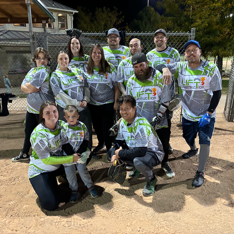 A group of people, including adults and one child, are posing for a photo on a baseball field. They  
