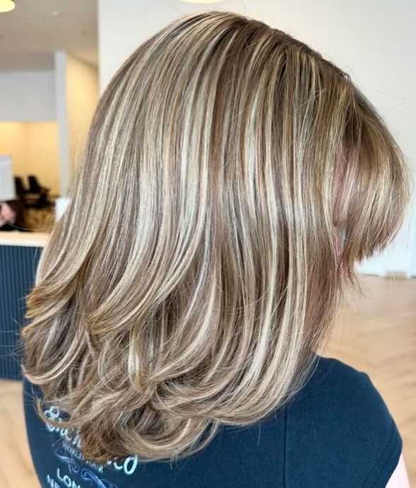 Side back view of layered blonde hair with soft highlights, styled with volume and movement in a modern salon setting.