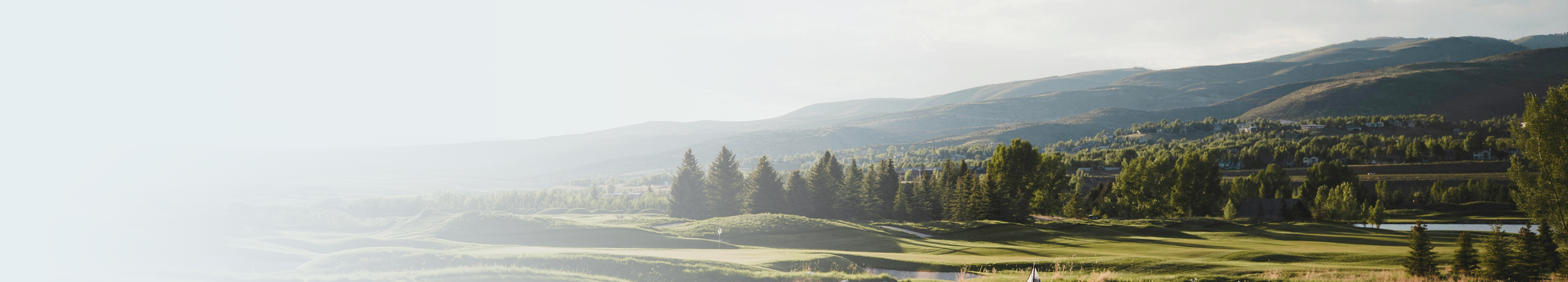 A golf course in the afternoon sun, with mountains and trees lining the perimeter.