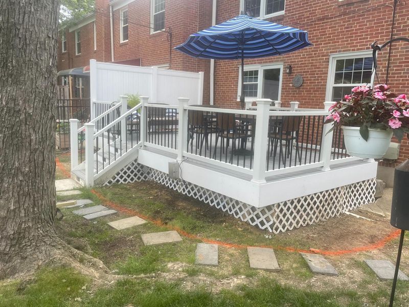 Backyard deck with white railing and seating area attached to brick home. The structure provides elevated outdoor space, showcasing professional installation that improves functionality, aesthetics, and usability of residential landscape design.