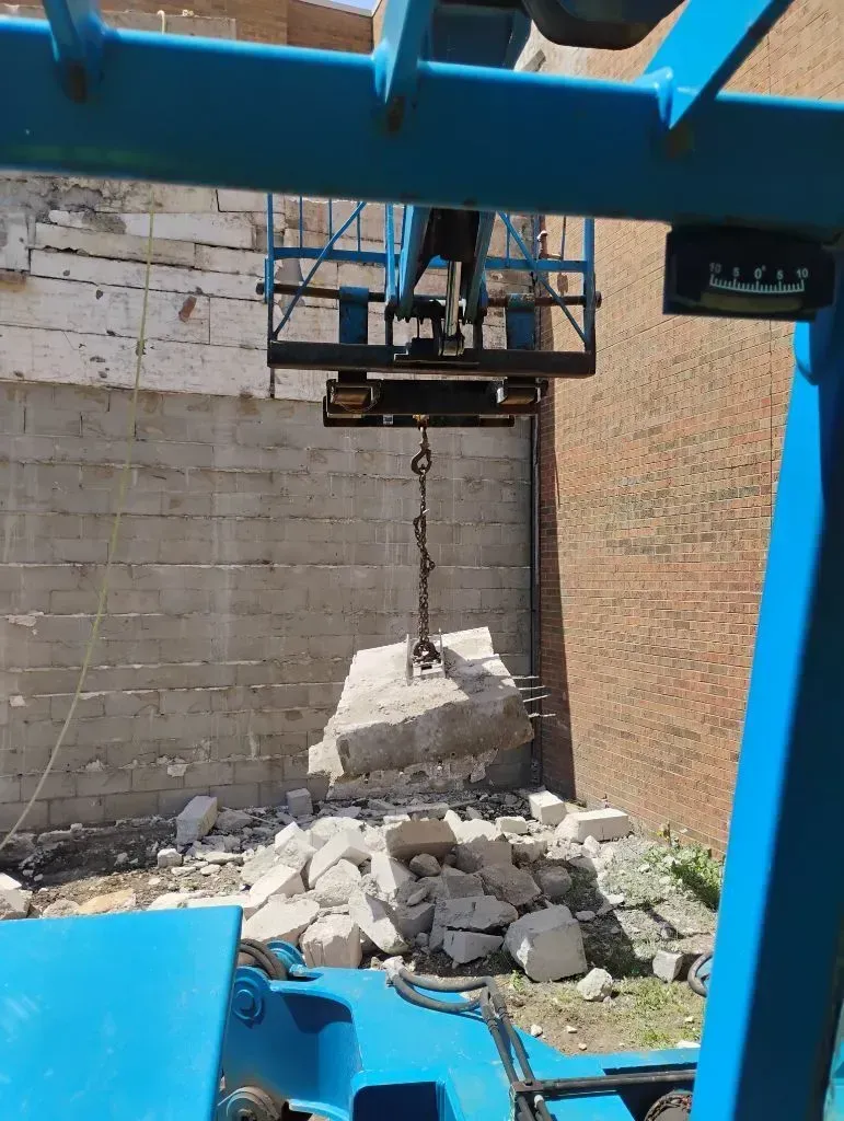 Heavy equipment lifting large concrete slab with chain during demolition, surrounded by broken debri 