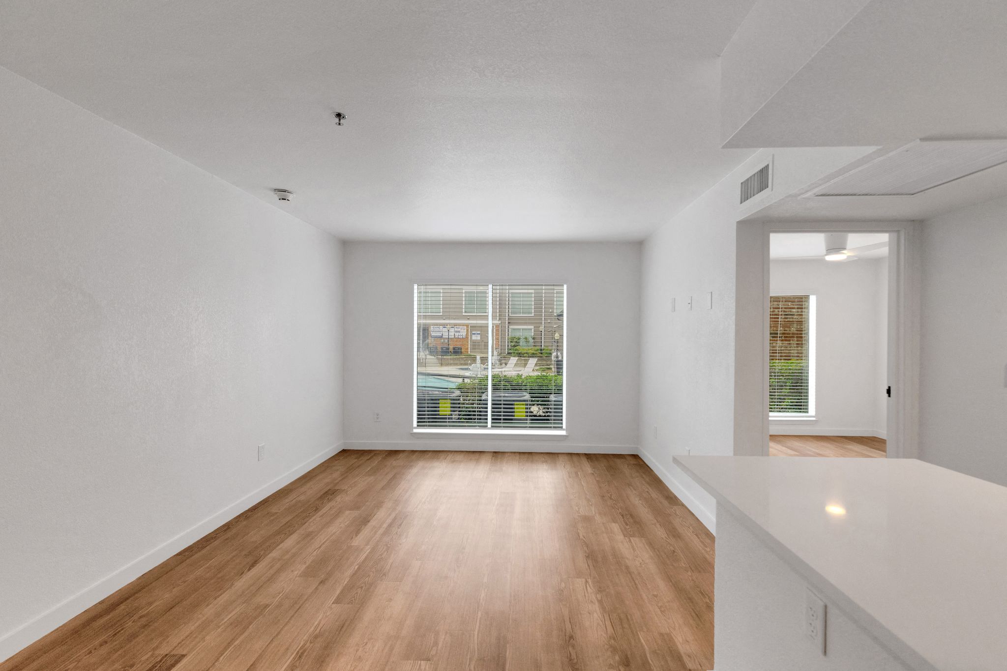 the living room and dining room of an apartment with wood floors and a large window 