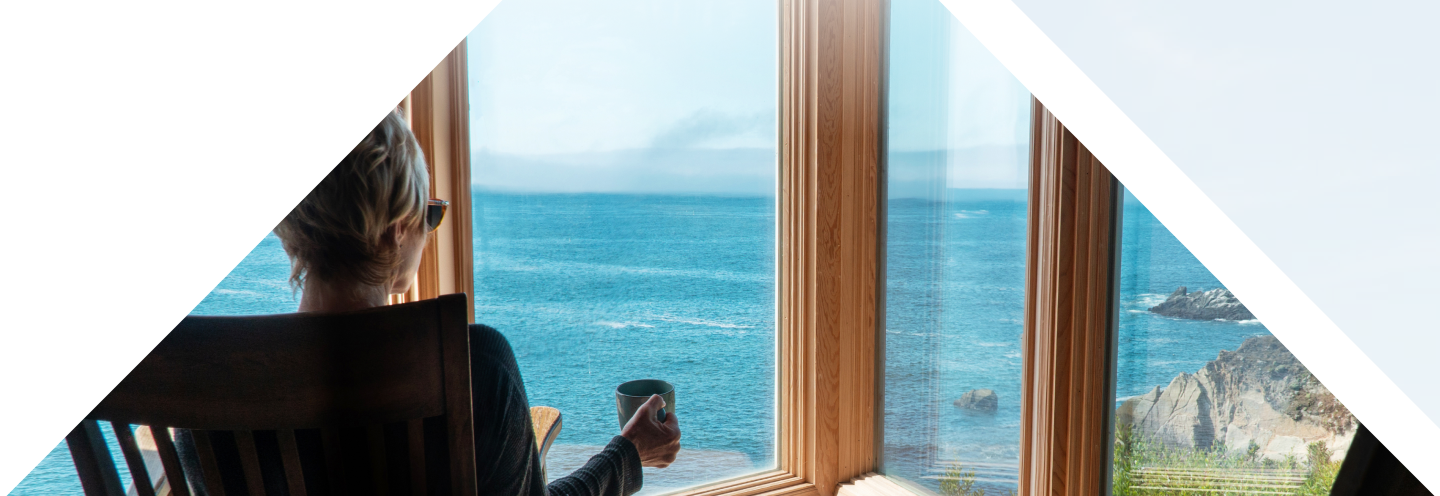 Woman relaxing with a cup of coffee while looking out at the ocean through her window.
