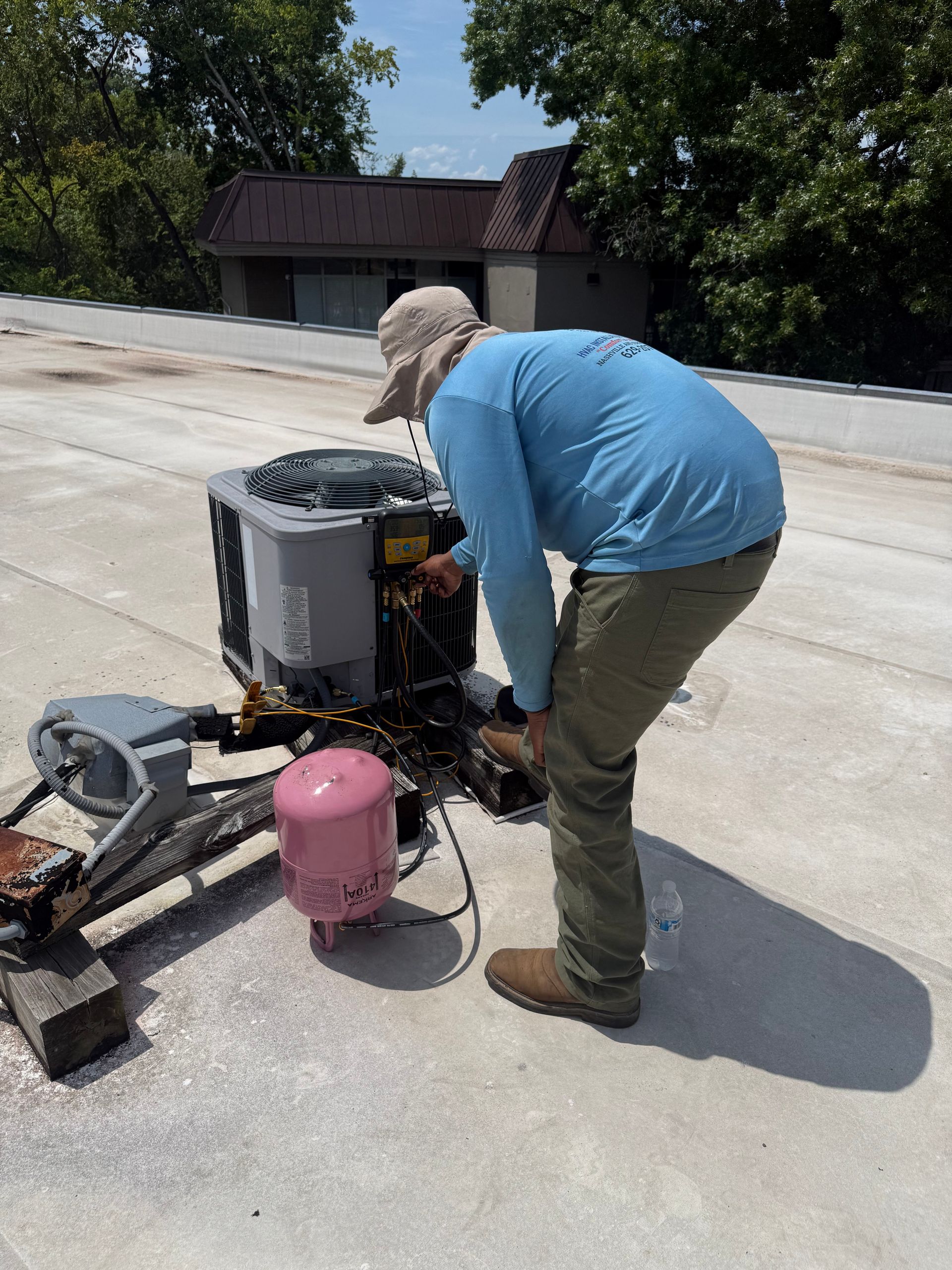 HVAC technician servicing a rooftop air conditioning condenser using digital gauges and connected ho 