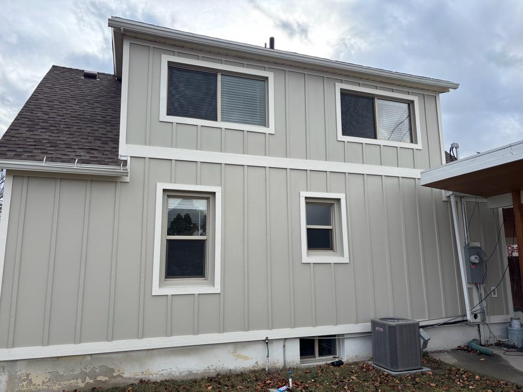 Exterior view of a light gray house with white trim around the windows and along the siding. There a 