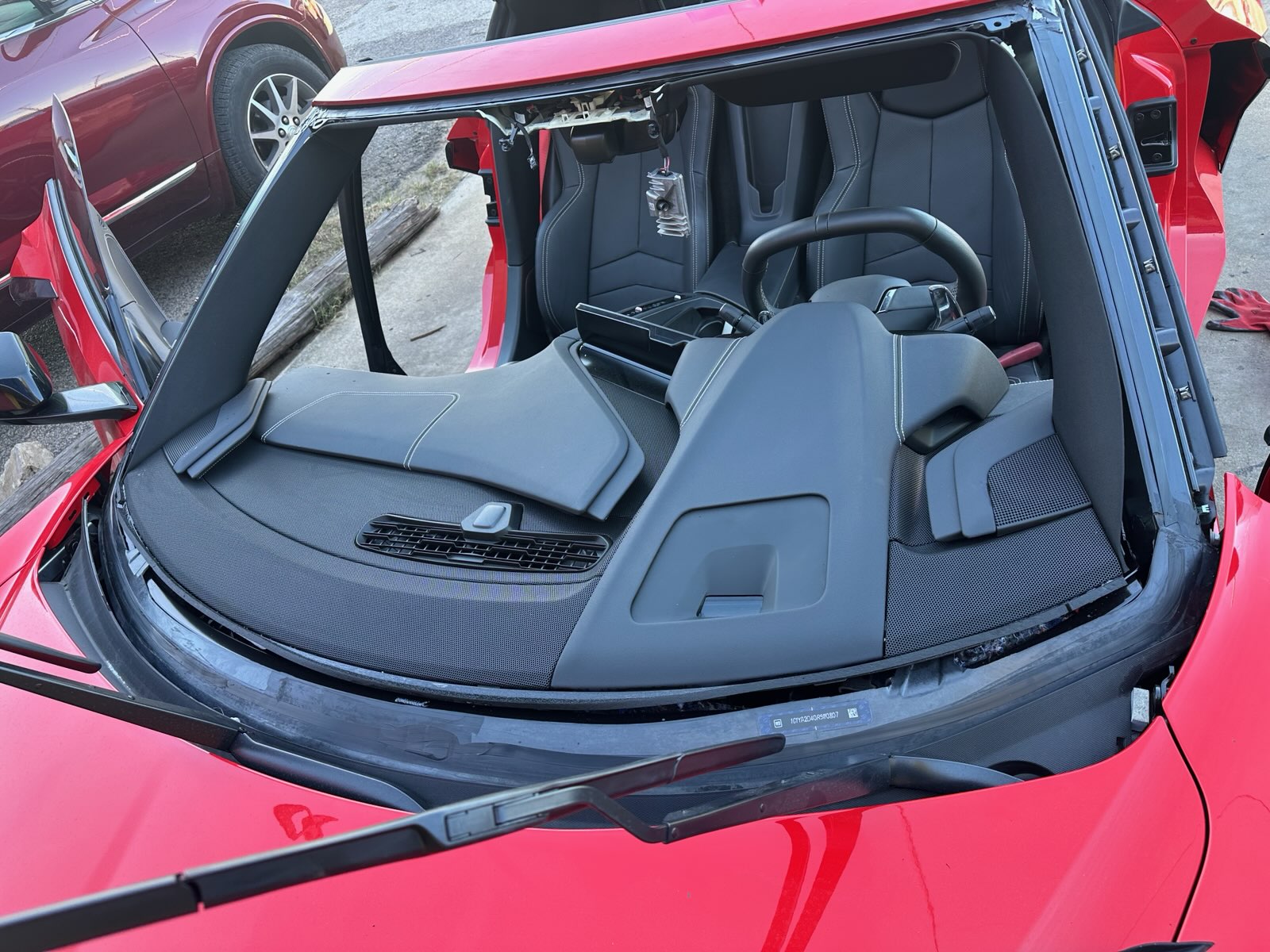 A red sports car is shown with the windshield removed and the opening prepared for new glass. The photo highlights the preparation involved in professional windshield replacement.