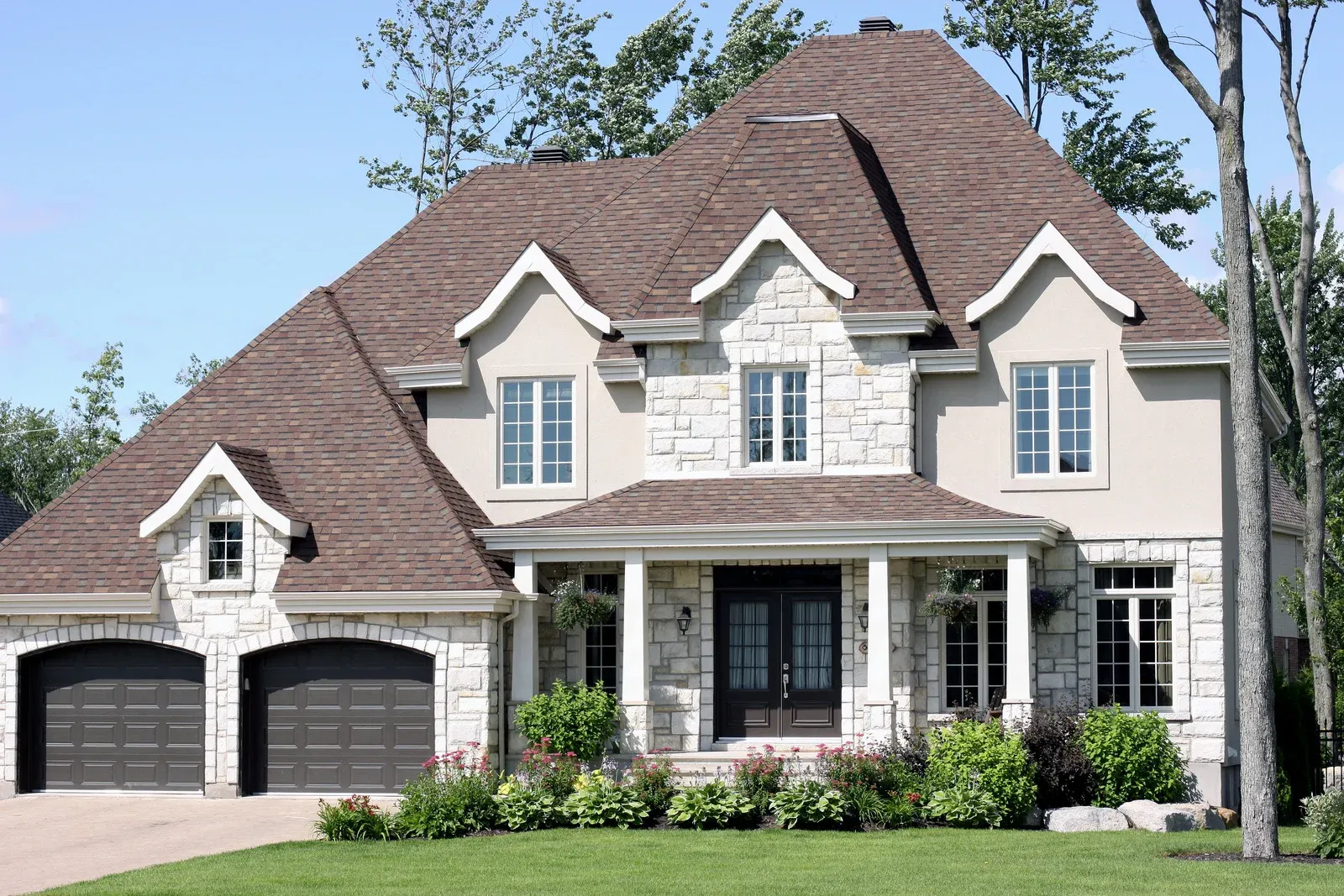 Large traditional luxury home with stone facade, multiple gables, landscaped front yard, double garage, and elegant architectural detailing, representing high-quality residential construction and classic suburban design excellence.
