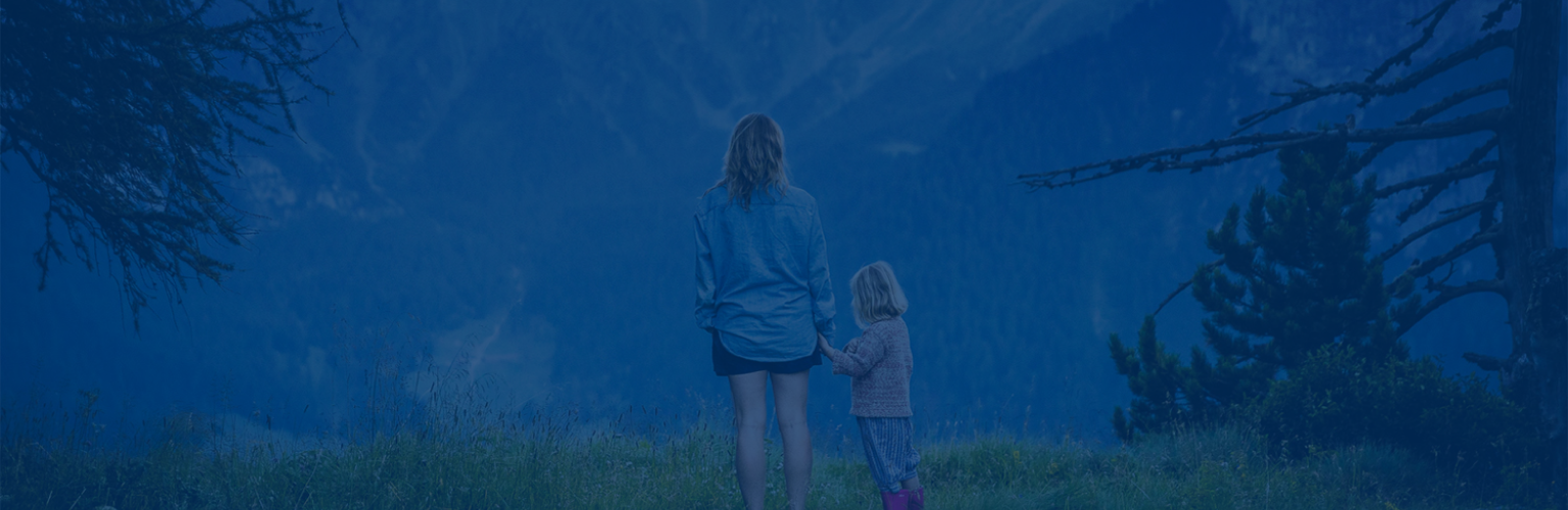 A mother and young daughter taking in the view of the mountains from a lookout point.