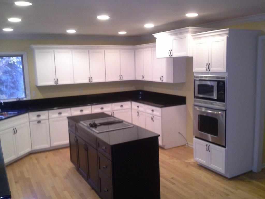 A modern kitchen featuring white cabinetry, black countertops, and a central island with built-in cooktop. Recessed lighting and stainless steel appliances enhance functionality and create a clean, contemporary design.