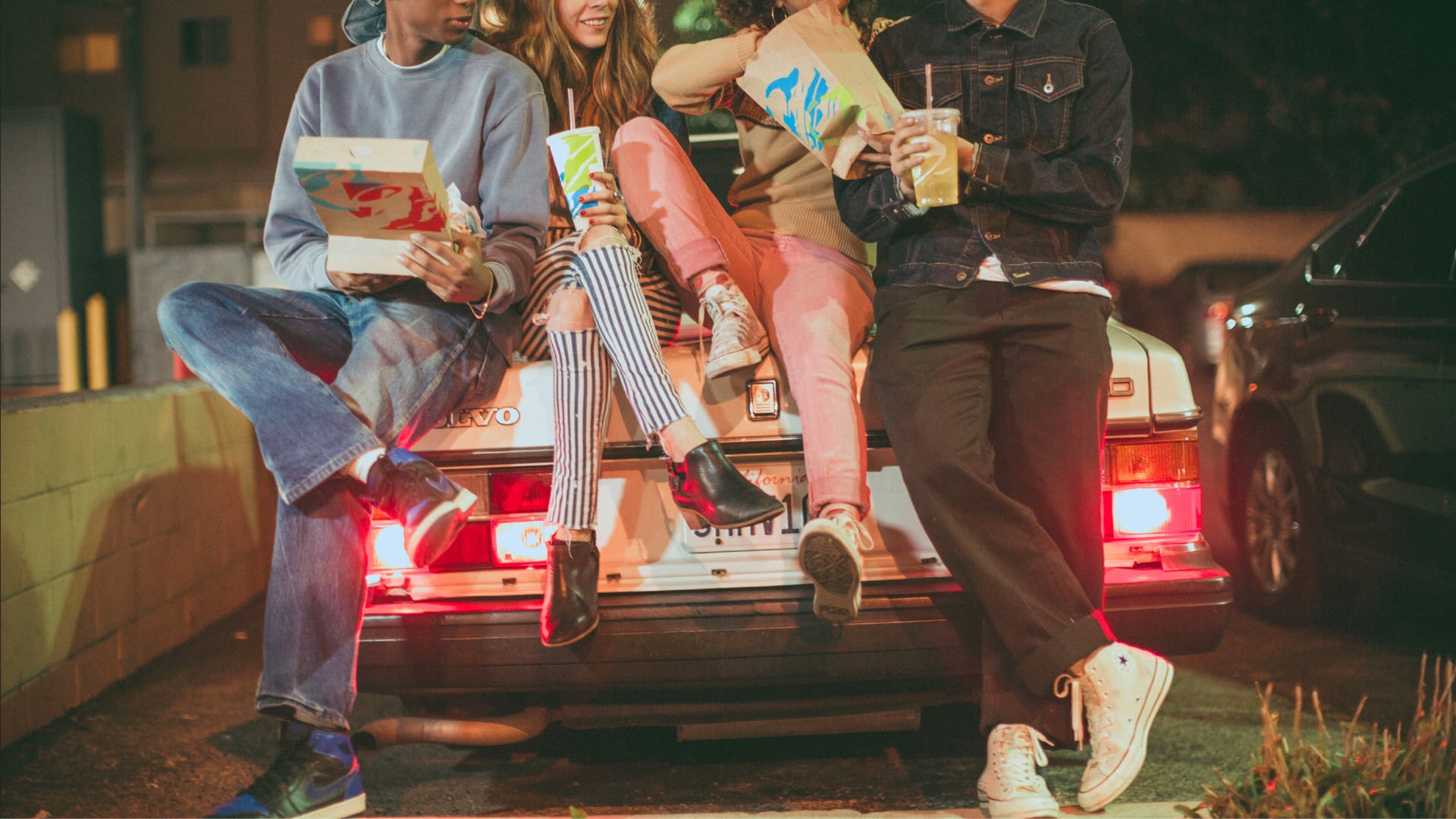 Drei junge Leute, die sich an den Kofferraum eines Autos lehnen und Tacos und Burritos von Taco Bell essen.