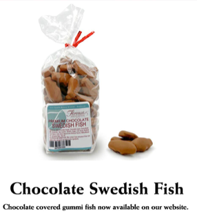This photograph features a bag of Florence's Exquisite Chocolates' "Premium Chocolate Swedish Fish," likely from their Rexburg, Idaho location. The clear bag showcases the chocolate-covered, fish-shaped candies, tied with a festive red ribbon. The product label clearly states "Premium Chocolate Swedish Fish" and includes a barcode. Several loose chocolate-covered Swedish Fish are scattered beside the bag, revealing their detailed fish shape and milk chocolate coating.