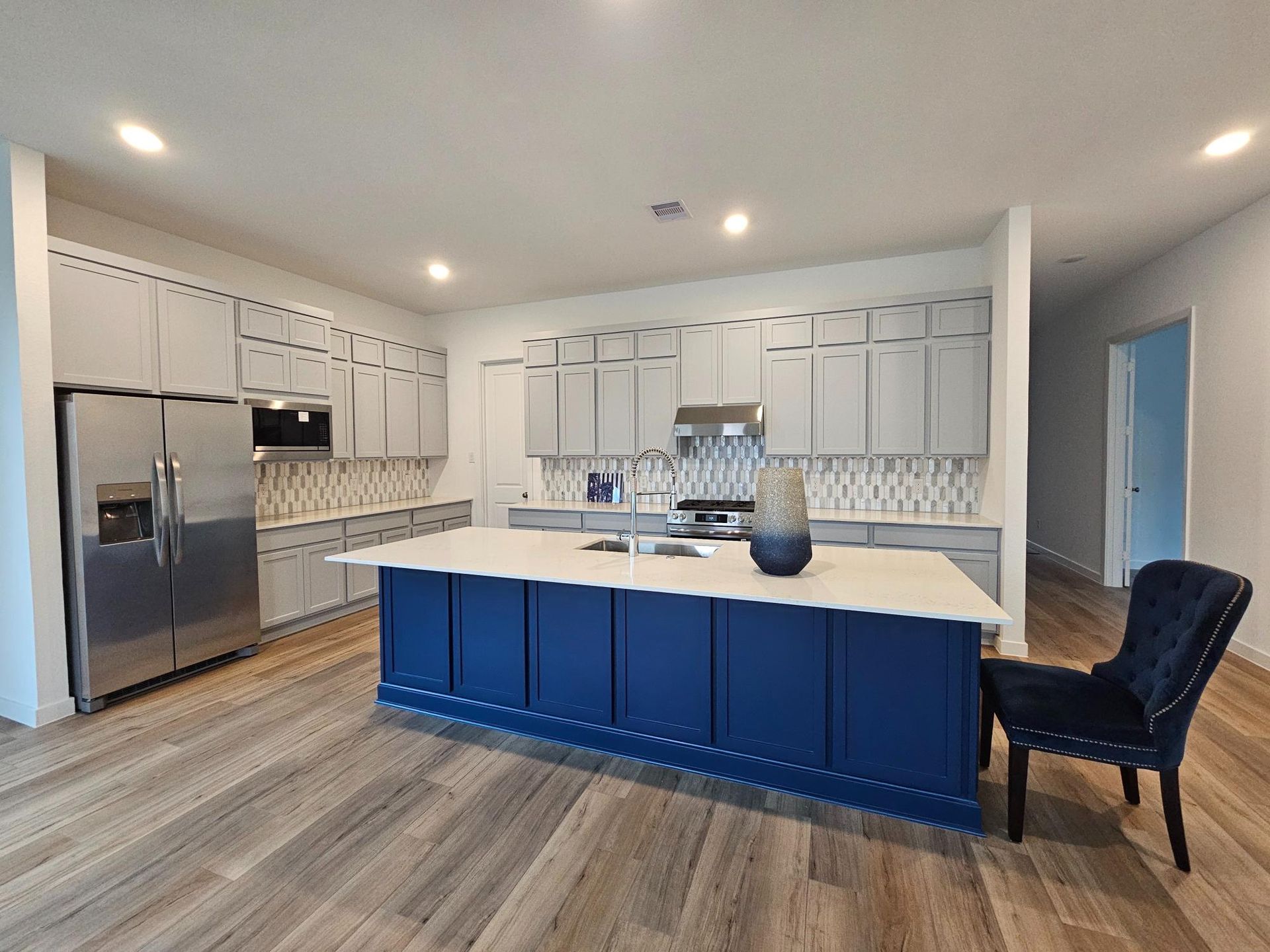 Contemporary kitchen featuring soft gray cabinetry with a bold navy blue island, white countertops, decorative backsplash, and open layout delivering stylish contrast and modern residential interior appeal.