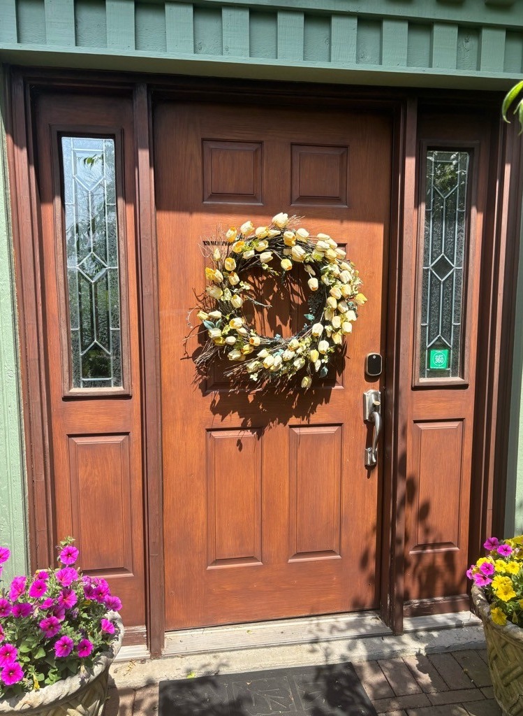 Residential wood-grain front entry door with a warm stained finish, featuring decorative glass sidelights on both sides and a classic raised-panel design. This entry door enhances curb appeal while allowing natural light into the home, combining traditional style with durability and security.