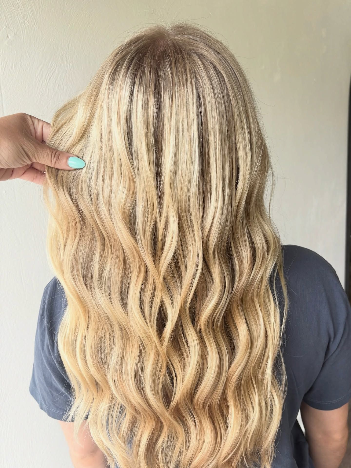 Back view of long blonde hair with soft beach waves and subtle highlights, styled professionally for a smooth natural salon finish.