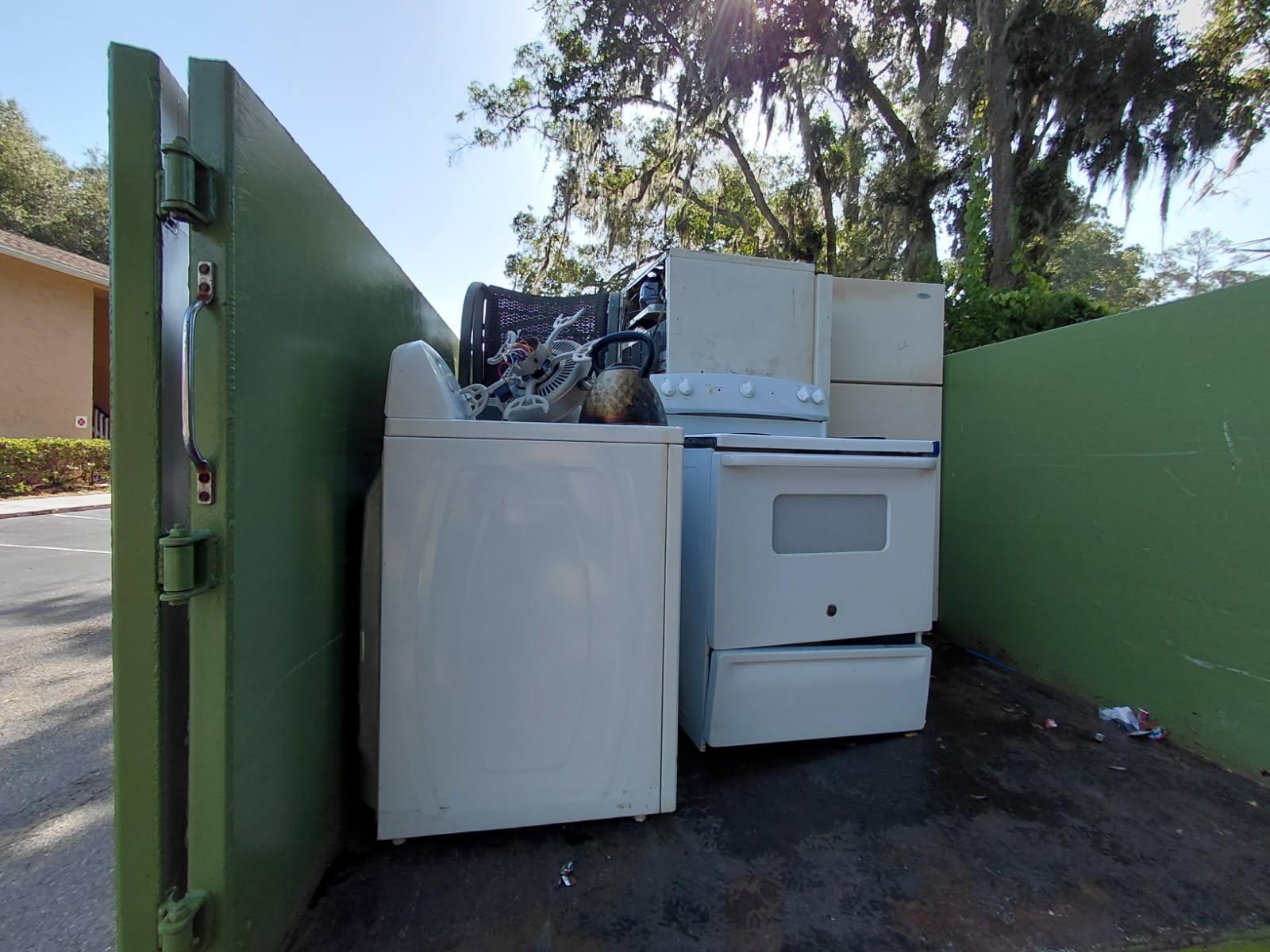 A white washing machine, stove, and refrigerator loaded into the back of a green JunkShot disposal t 
