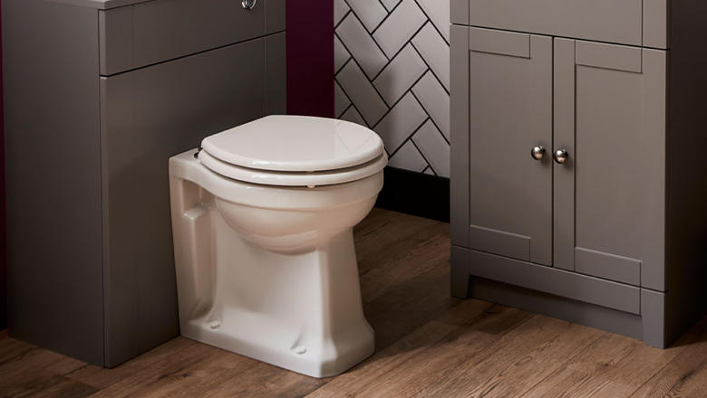 A white classic style back to wall toilet against a dark grey vanity unit in a bathroom with wood floor and herringbone wall tiles