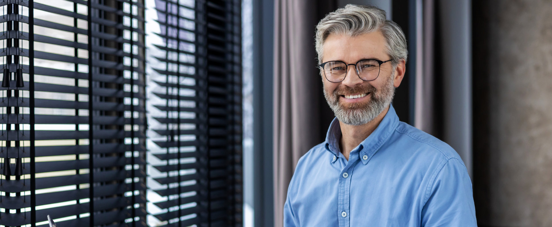 A close-up shot of a smiling middle-aged man with salt-and-pepper hair and a beard, wearing glasses  