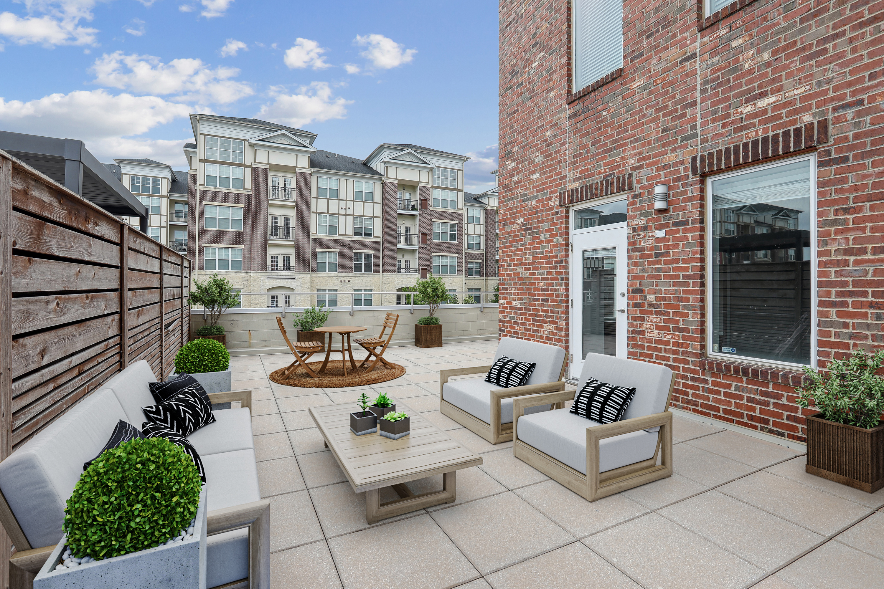 A patio with a white couch, a wooden table, and a brick building in the background.