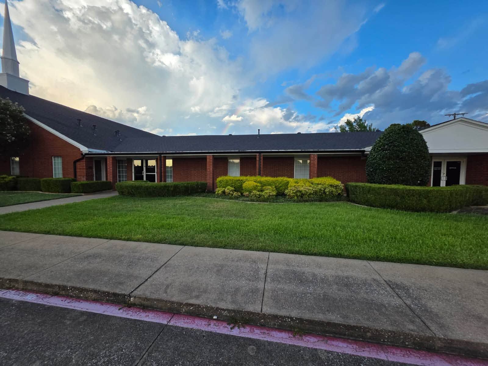 Commercial roofing project featuring a brick facility with dark shingle roofing, neatly trimmed land 