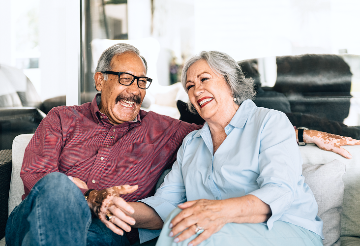 An elderly couple laughing together on the couch.