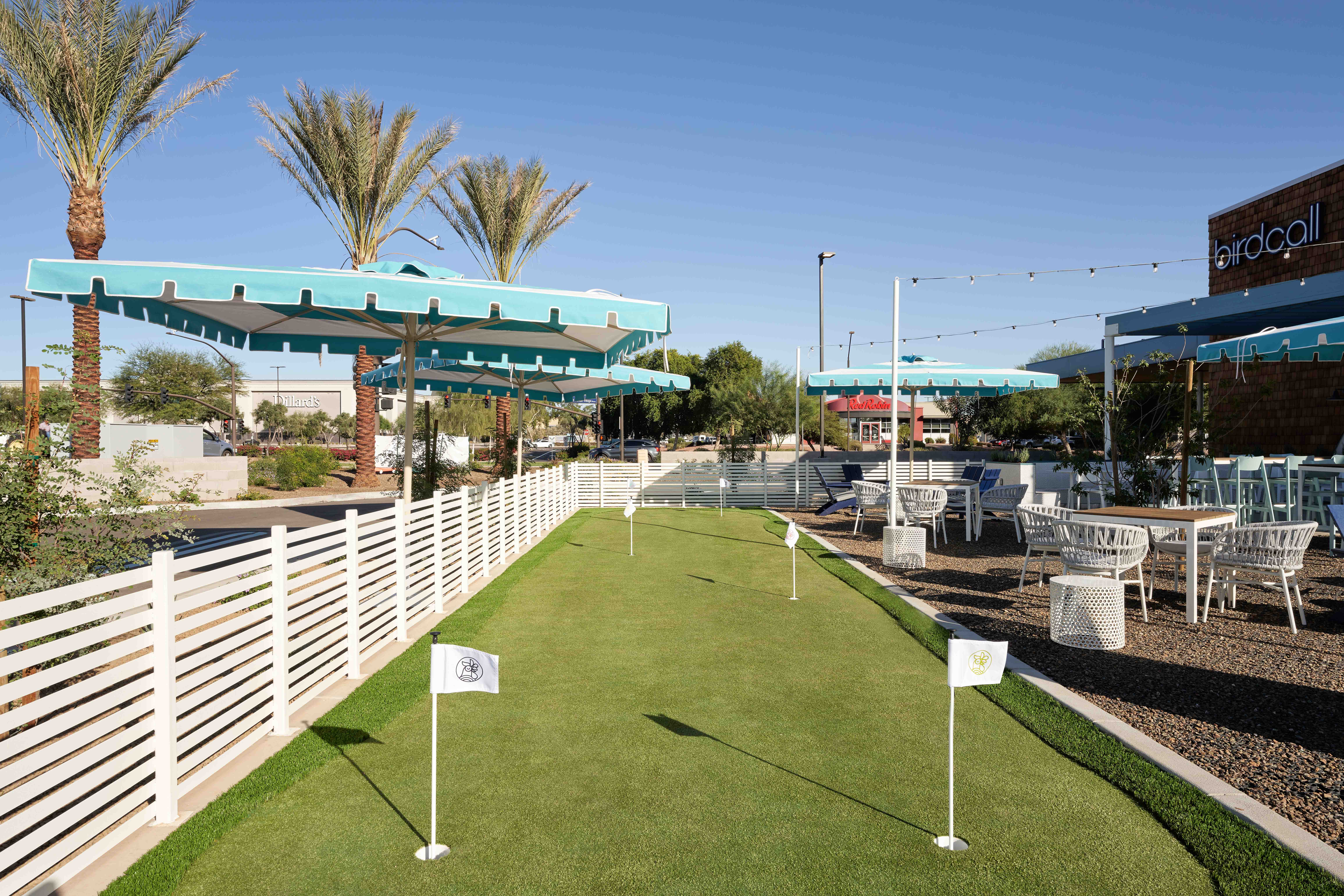 View of Birdcall SanTan's putting green, flanked with umbrellas and palm trees.