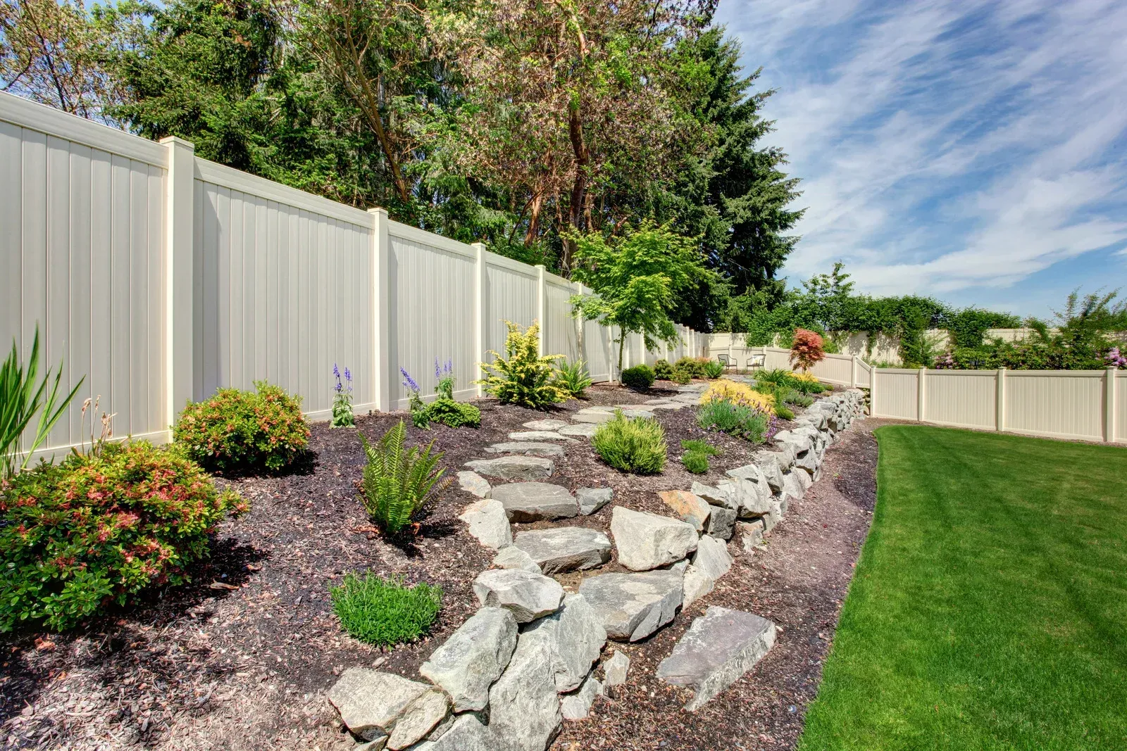 Well-designed backyard landscape featuring decorative stone pathway, mulch beds, ornamental plants,  