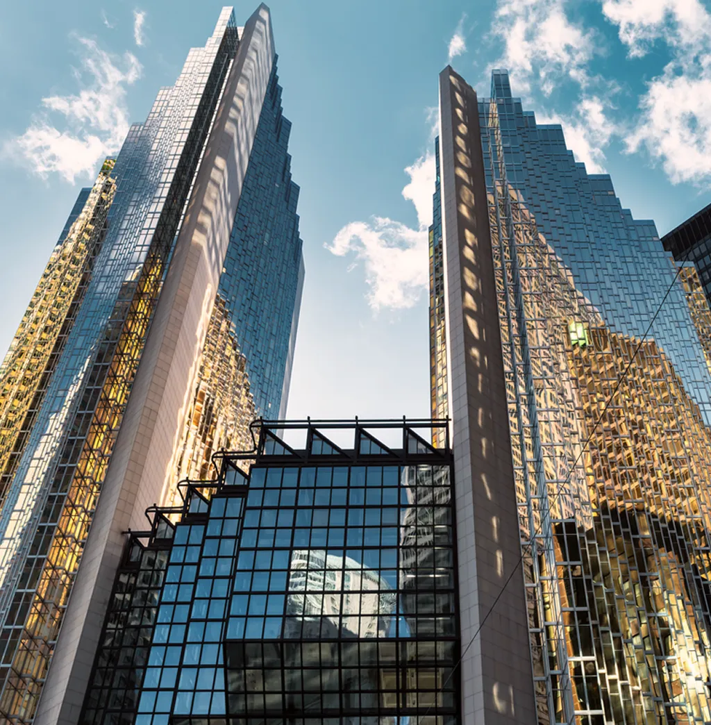Upward view of modern glass and steel skyscrapers against a bright blue sky.