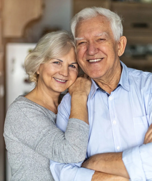 Close-up portrait of a happy senior couple embracing and smiling warmly into the camera inside a home environment.