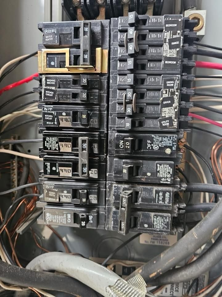 Detailed view of circuit breaker panel with labeled switches, wiring, and connections, showing organized but used electrical distribution system with multiple breakers controlling different household circuits.