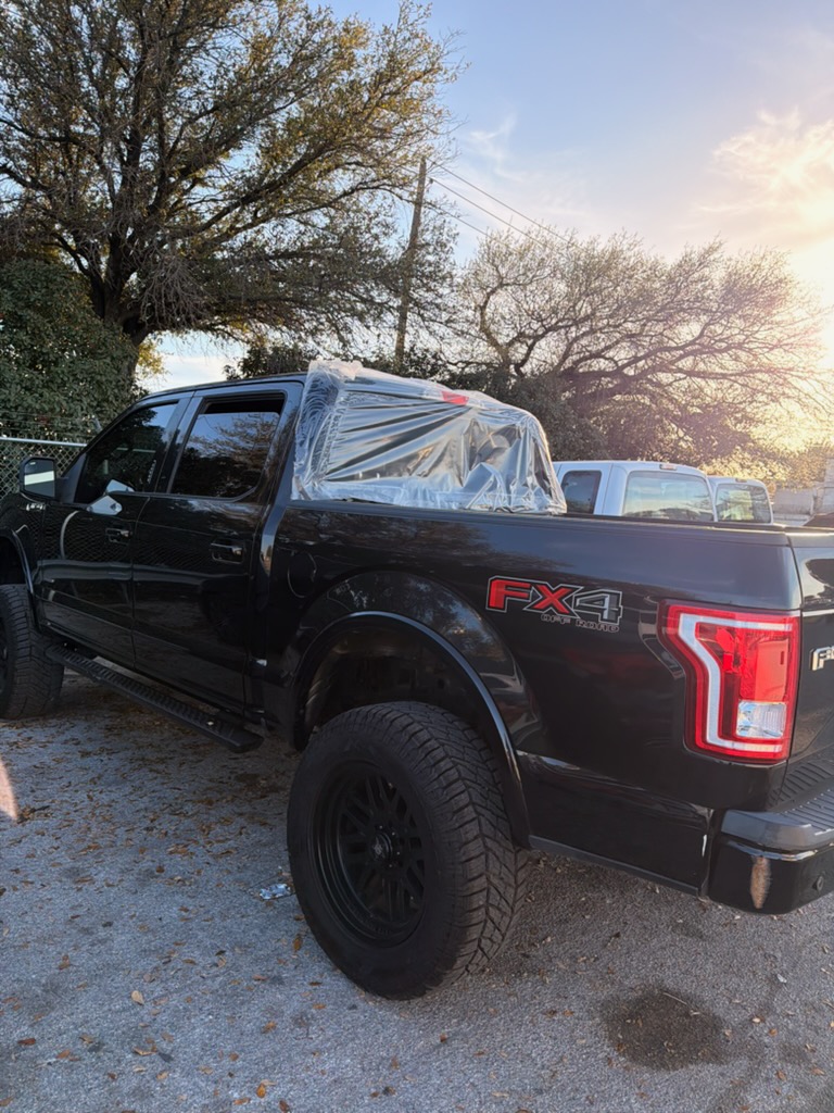 A black Ford F-150 with protective plastic covering the rear cab window area before auto glass service. The photo illustrates rear window replacement work for pickup trucks.