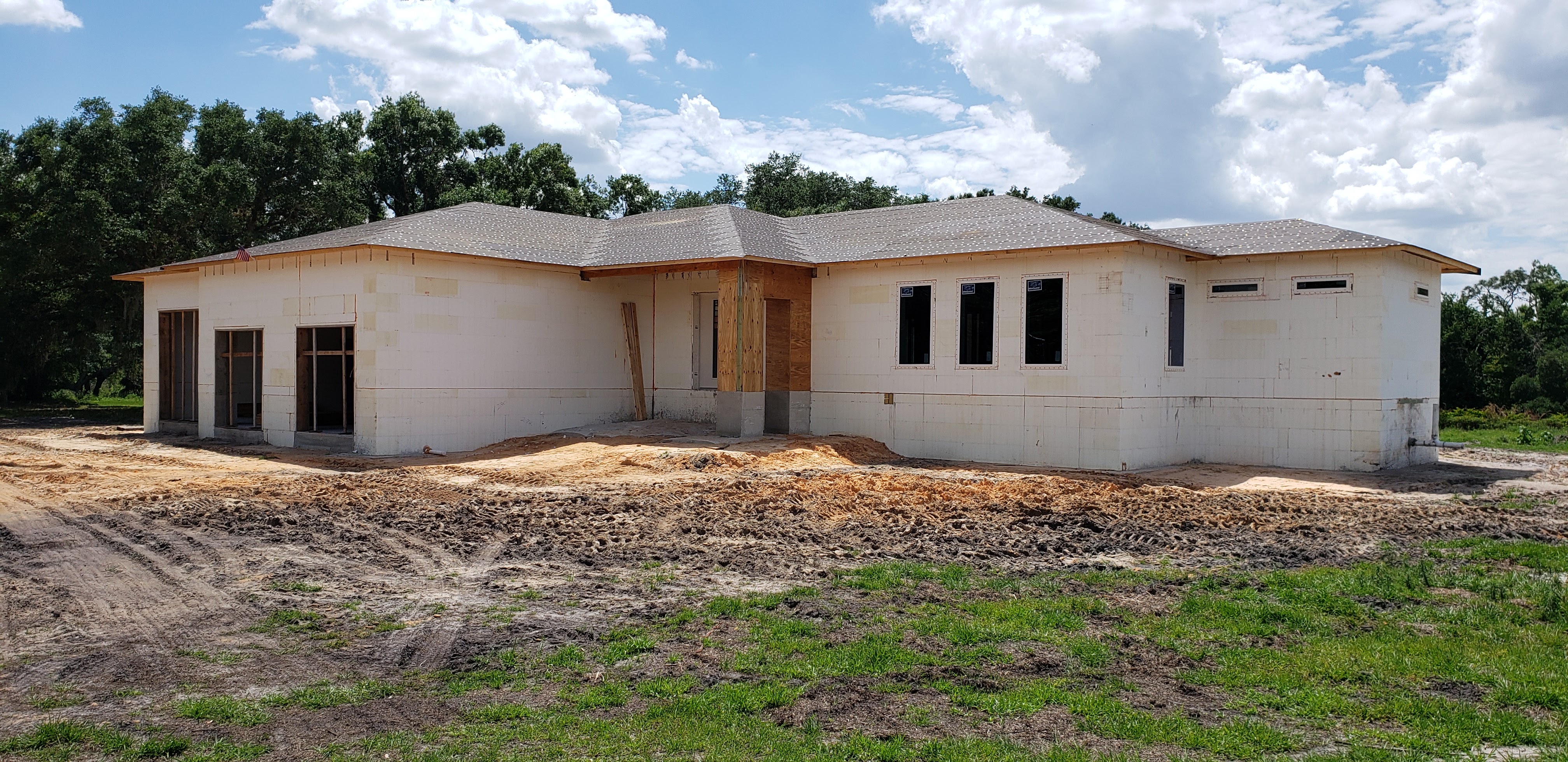A house under construction is shown with its white foam block walls and a gray shingled roof. The wi 