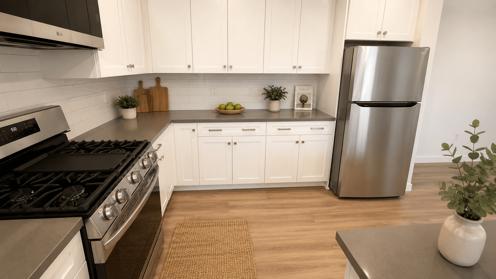 A modern kitchen with a stainless steel refrigerator, wooden floors, and white cabinets.