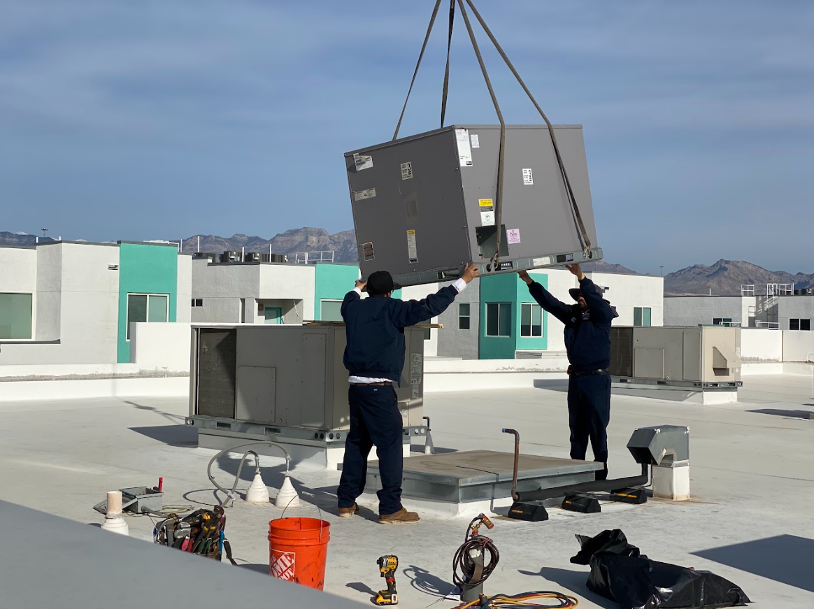 Crew installing large rooftop HVAC unit with crane. 