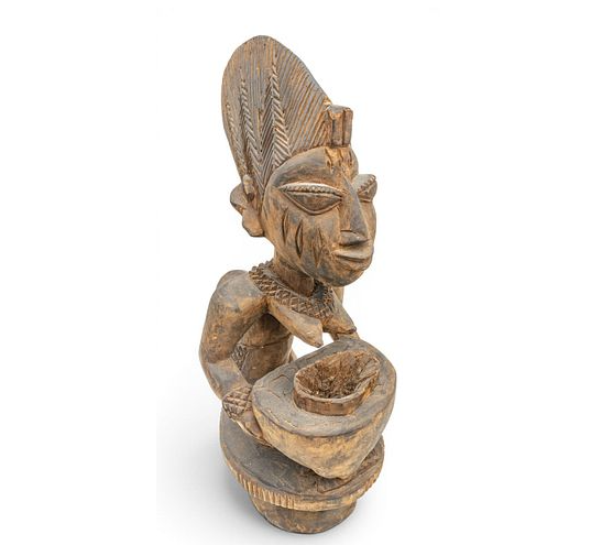 Semi nude female kneeling with a bowl in her hands. A child in a carrier upon her back.