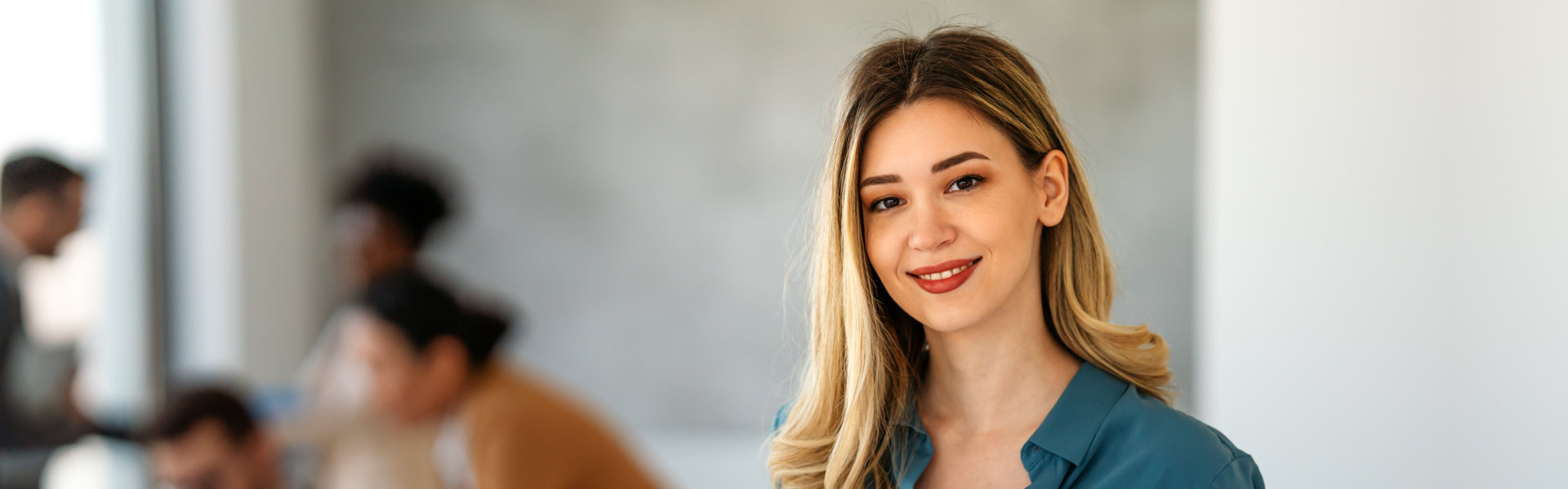 A close-up shot captures a smiling woman with blonde hair styled in loose waves. She is wearing a te 