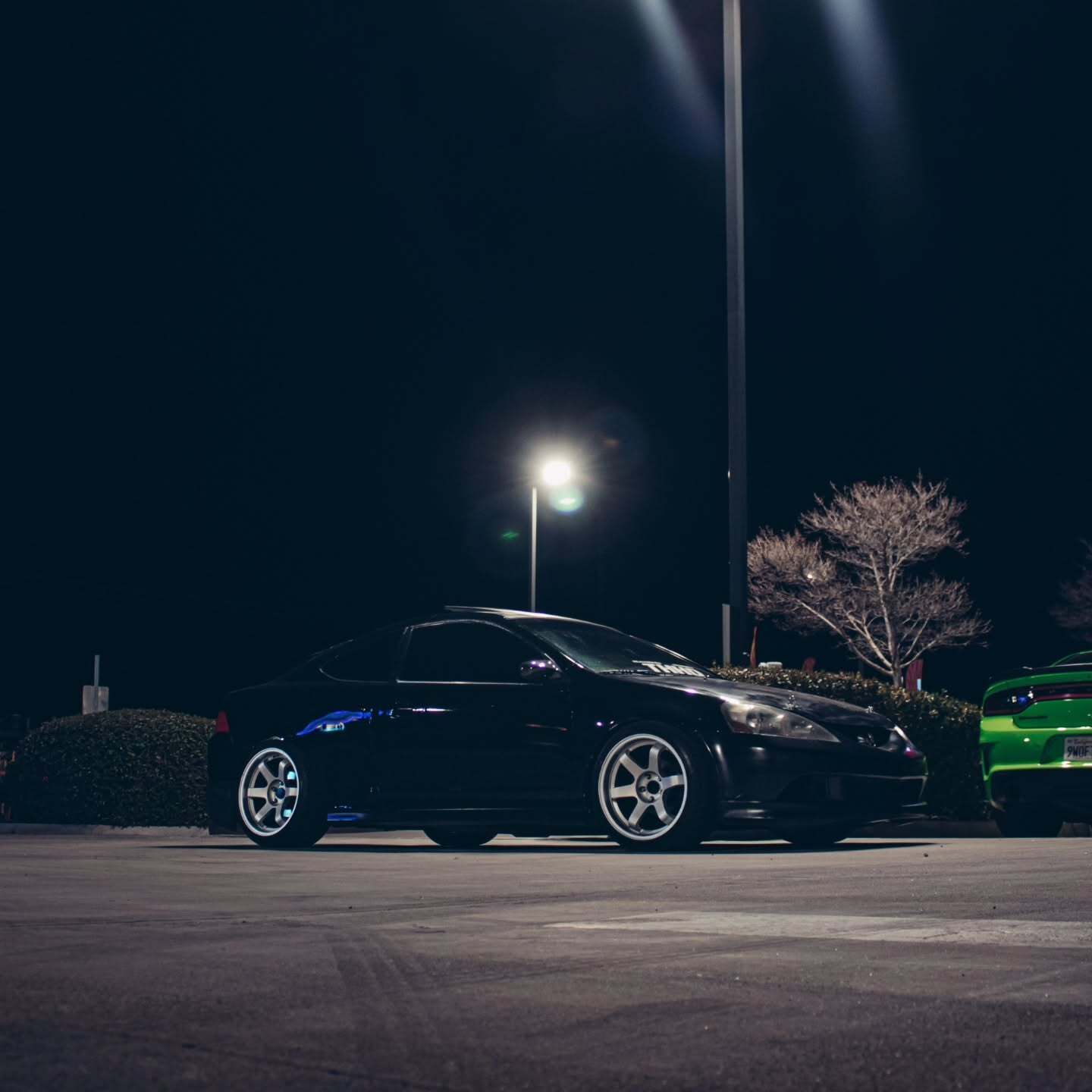 Black Honda coupe photographed under bright parking lot lights during a nighttime car meet. The lowe 